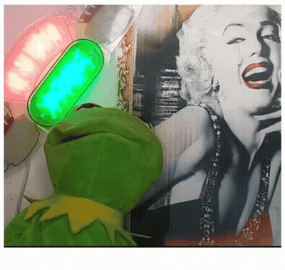 A Green Kermit Frog Is Standing In Front Of A Picture Of Marilyn Monroe GIF