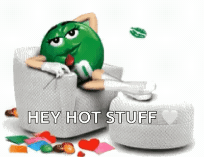 A Green M & M Is Laying In A Chair With Hearts Around Him And Says Hey Hot Stuff . GIF