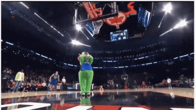 A Green Mascot Stands On A Basketball Court In Front Of A Scoreboard That Says Coca Cola GIF