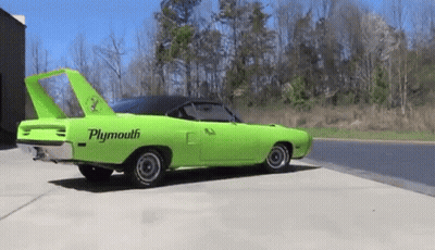A Green Plymouth Superbird Is Parked On The Side Of The Road . GIF