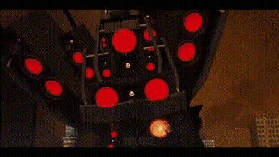 A Green Robot Is Holding A Gun In Front Of A City At Night . GIF