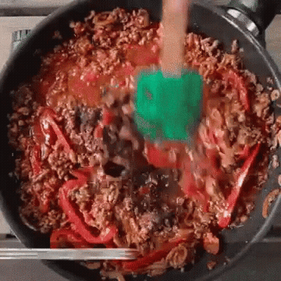 A Green Spatula Is Stirring A Pan Of Food GIF