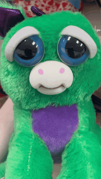A Green Stuffed Animal With Blue Eyes And A Purple Heart On Its Chest GIF