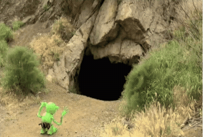 A Green Toy Is Standing In Front Of A Cave Entrance GIF