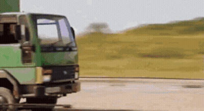 A Green Truck Is Driving Down A Dirt Road In The Countryside . GIF