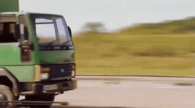 A Green Truck Is Driving Down A Road With Grass In The Background GIF