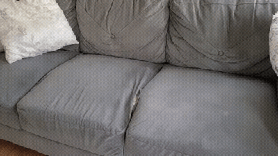 A Grey Leather Couch With White Pillows On It GIF