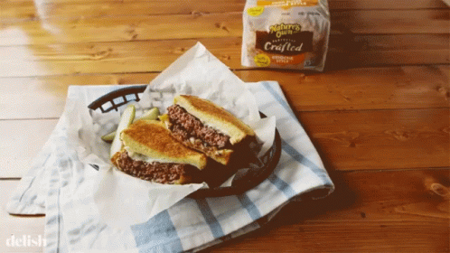 A Grilled Cheese Sandwich In A Basket On A Table Next To A Bag Of Nature 'S Own Bread GIF