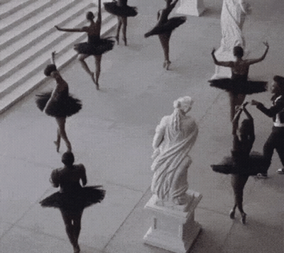 A Group Of Ballerinas In Black Tutus Are Dancing In Front Of A Statue GIF