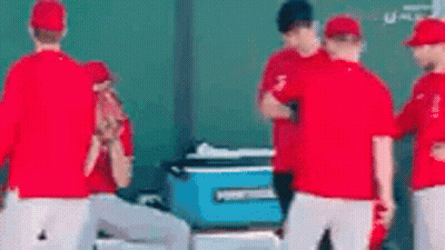 A Group Of Baseball Players Are Standing Around A Blue Cooler On The Field . GIF