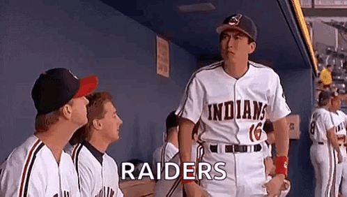 A Group Of Baseball Players Are Standing In A Dugout And One Of Them Is Wearing A Raiders Uniform . GIF