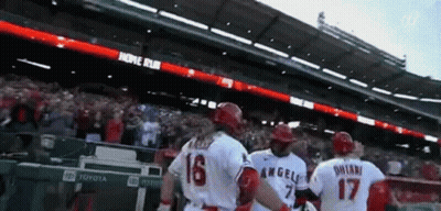 A Group Of Baseball Players Are Standing In A Stadium With A Banner That Says Home Run GIF