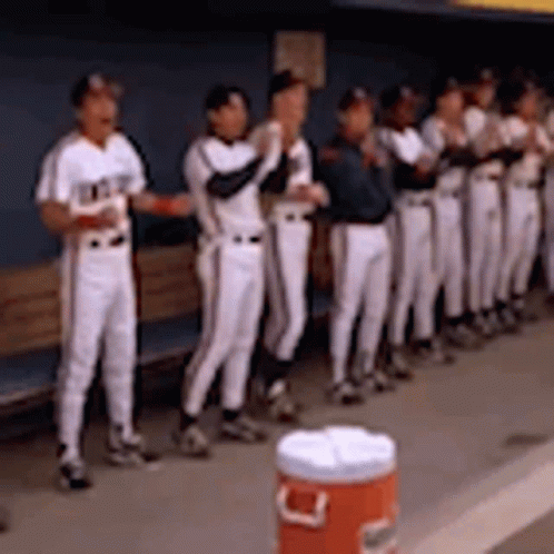 A Group Of Baseball Players Standing In A Dugout With A Cooler In The Foreground . GIF