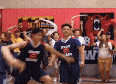 A Group Of Basketball Players Are Dancing On A Court While A Crowd Watches . GIF
