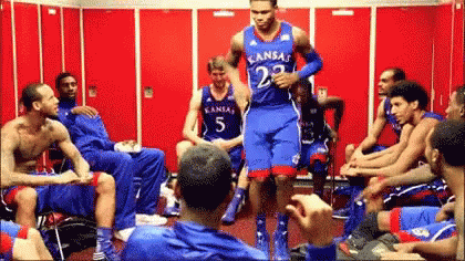 A Group Of Basketball Players Are Sitting In A Locker Room And One Has Kansas On His Jersey GIF