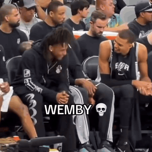 A Group Of Basketball Players Are Sitting In The Stands And One Of Them Is Wearing A Hoodie That Says Wemby GIF
