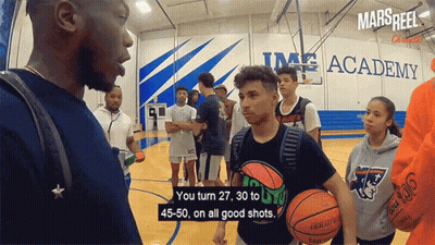 A Group Of Basketball Players Are Standing On A Court In Front Of A Sign That Says Mars Reel GIF