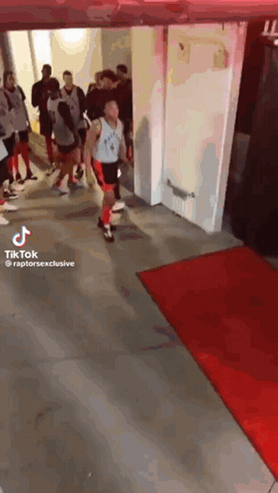 A Group Of Basketball Players Are Walking Through A Hallway With A Red Carpet . GIF