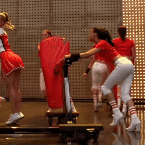 A Group Of Cheerleaders Are Standing On A Stage Holding A Red Bag GIF