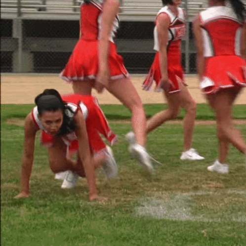 A Group Of Cheerleaders In Red Uniforms Are Crawling On The Field GIF