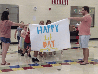 A Group Of Children Are Holding Up A Sign That Says Happy 1St Day GIF