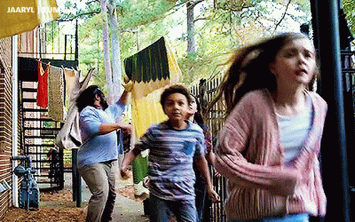 A Group Of Children Are Running Down A Sidewalk In Front Of A Building With Clothes Hanging On A Clothesline . GIF