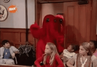 A Group Of Children Are Sitting In A Room With A Red Monster Mascot . GIF