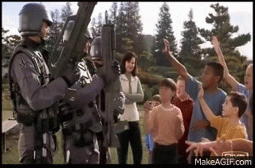 A Group Of Children Are Standing Around A Soldier Holding A Rifle . GIF