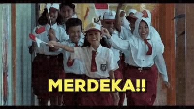 A Group Of Children In School Uniforms Are Walking Down A Hallway Holding Flags And A Sign That Says Merdeka . GIF