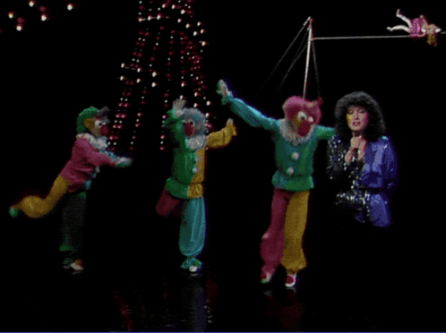 A Group Of Clowns Are Performing On Stage With A Woman Singing Into A Microphone GIF