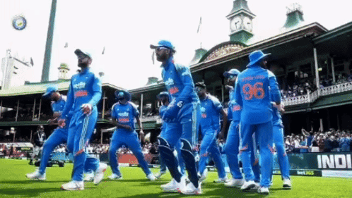 A Group Of Cricket Players Are Walking On A Field In Front Of A Building With The Number 96 On Their Jersey . GIF