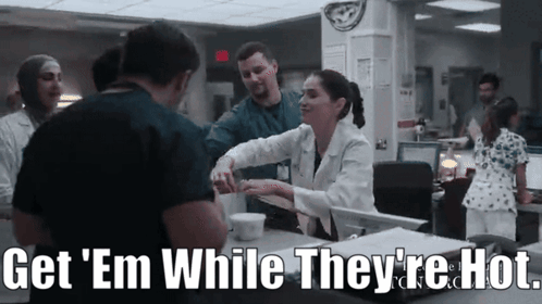 A Group Of Doctors And Nurses Are Standing Around A Counter With The Words Get ' Em While They 'Re Hot GIF