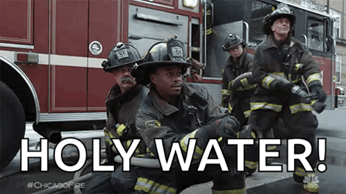A Group Of Firefighters Are Kneeling In Front Of A Fire Truck And Holding Hoses . GIF