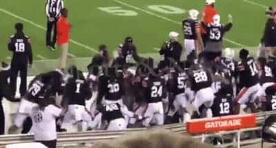 A Group Of Football Players Are Fighting On A Field In Front Of A Gatorade Stand . GIF