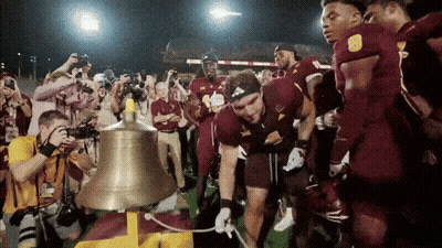 A Group Of Football Players Are Gathered Around A Bell GIF
