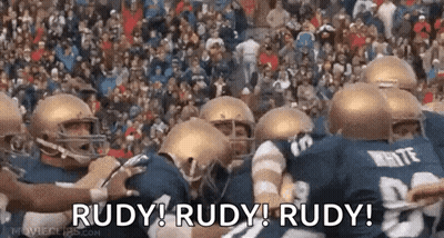 A Group Of Football Players Are Huddled Together With The Words Rudy ! Rudy ! Rudy ! Written On The Bottom GIF