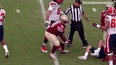 A Group Of Football Players Are Playing A Game On A Field With A Referee Standing Between Them . GIF