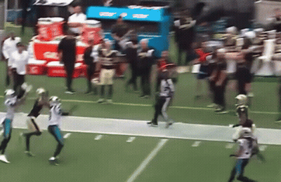 A Group Of Football Players Are Playing On A Field With Gatorade Coolers In The Background . GIF