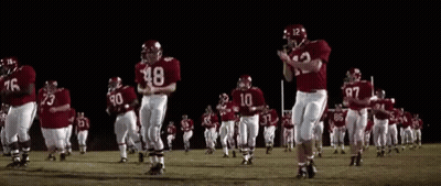 A Group Of Football Players Are Running On A Field At Night GIF