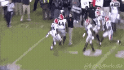 A Group Of Football Players Are Running On A Field While A Referee Watches . GIF