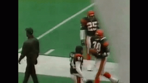 A Group Of Football Players Are Running On A Field With A Referee . GIF
