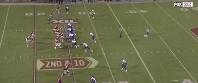 A Group Of Football Players Are Running On A Field With A Referee . GIF