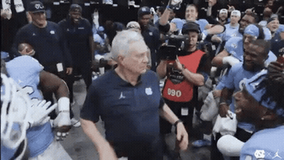 A Group Of Football Players Are Standing Around A Man . GIF