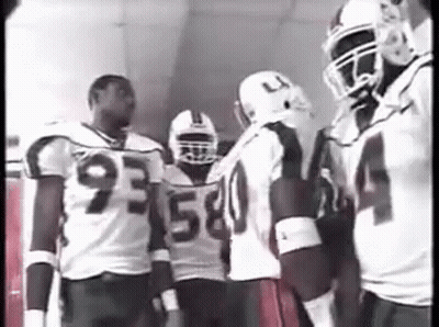 A Group Of Football Players Are Standing In A Hallway Talking To Each Other . GIF