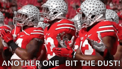 A Group Of Football Players Are Standing In A Line With The Words `` Another One Bit The Dust '' Written Above Them . GIF