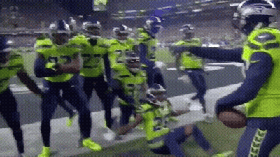 A Group Of Football Players Are Standing On A Field Holding A Ball . GIF