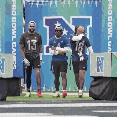 A Group Of Football Players Are Standing On A Field In Front Of A Sign That Says Pro Bowl Games GIF