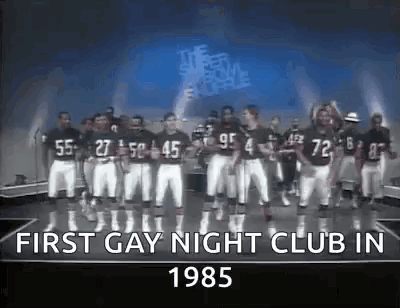 A Group Of Football Players Are Standing On A Stage In Front Of A Sign That Says First Gay Night Club In 1985 . GIF