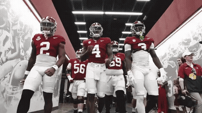 A Group Of Football Players Are Walking Down A Hallway GIF