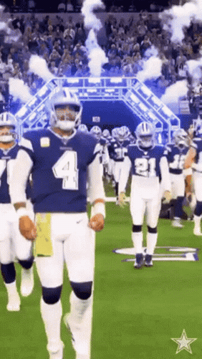 A Group Of Football Players Are Walking On A Field With Smoke Coming Out Of The Tunnel . GIF